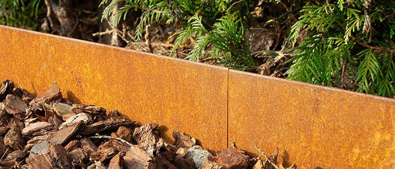 Cortenstalen kantopsluiting tussen een border met boomschors en groenblijvende beplanting.